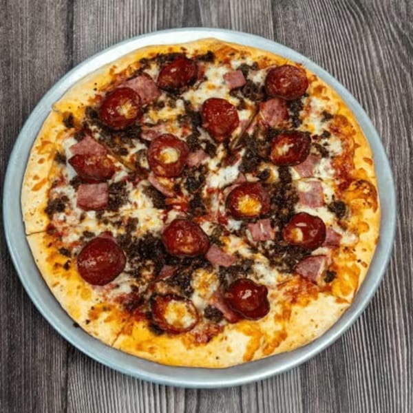Whole pizza with pepperoni, ground beef, and ham on a metal pan over a wooden table.