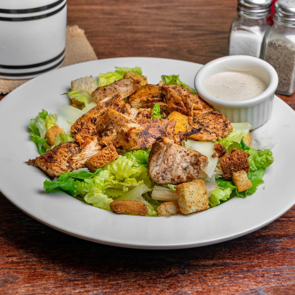 Grilled chicken Caesar salad with croutons and dressing on a white plate at Ricco's Pizza.