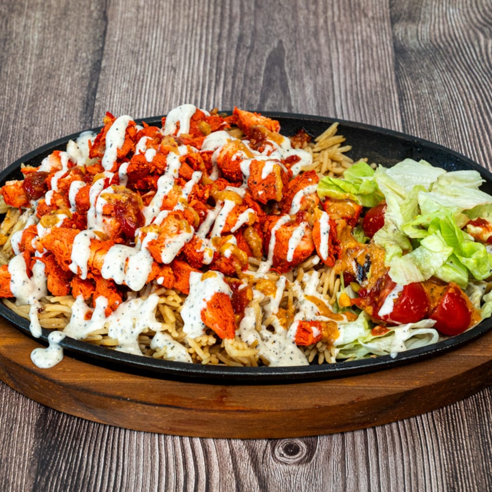 Ricco's Pizza's sizzling platter of chicken tikka, rice, lettuce, and tomatoes, drizzled with sauce.