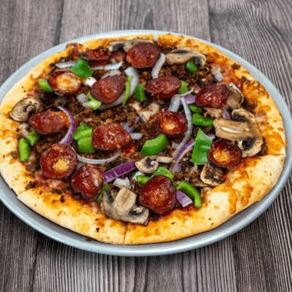 A whole pizza with pepperoni, ground meat, mushrooms, green peppers, and onions on a wooden table.