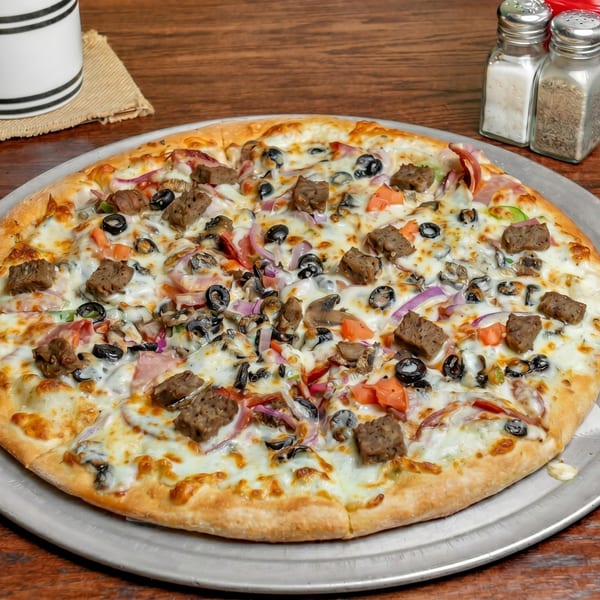 A whole pizza with sausage, olives, red onions, and bell peppers on a metal tray.