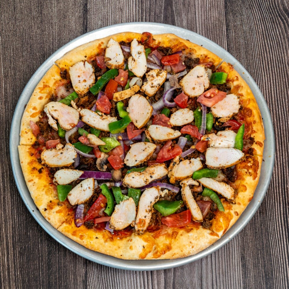 Ricco's Pizza with chicken, green peppers, red onions, and tomatoes on a wooden table.