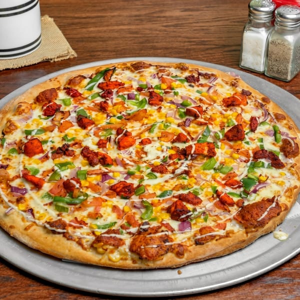 A large, colorful pizza with chicken, corn, peppers, and onions on a metal tray.