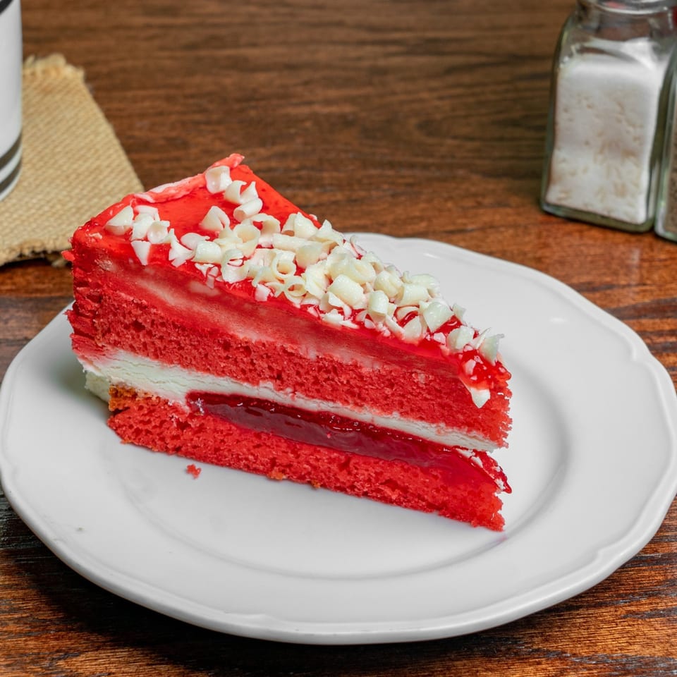 A slice of red velvet cake with white chocolate shavings on a white plate.